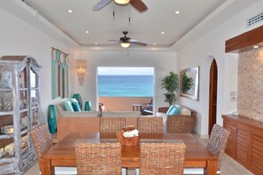 Uma sala de jantar com vista para o oceano, móveis de vime e um ventilador de teto.