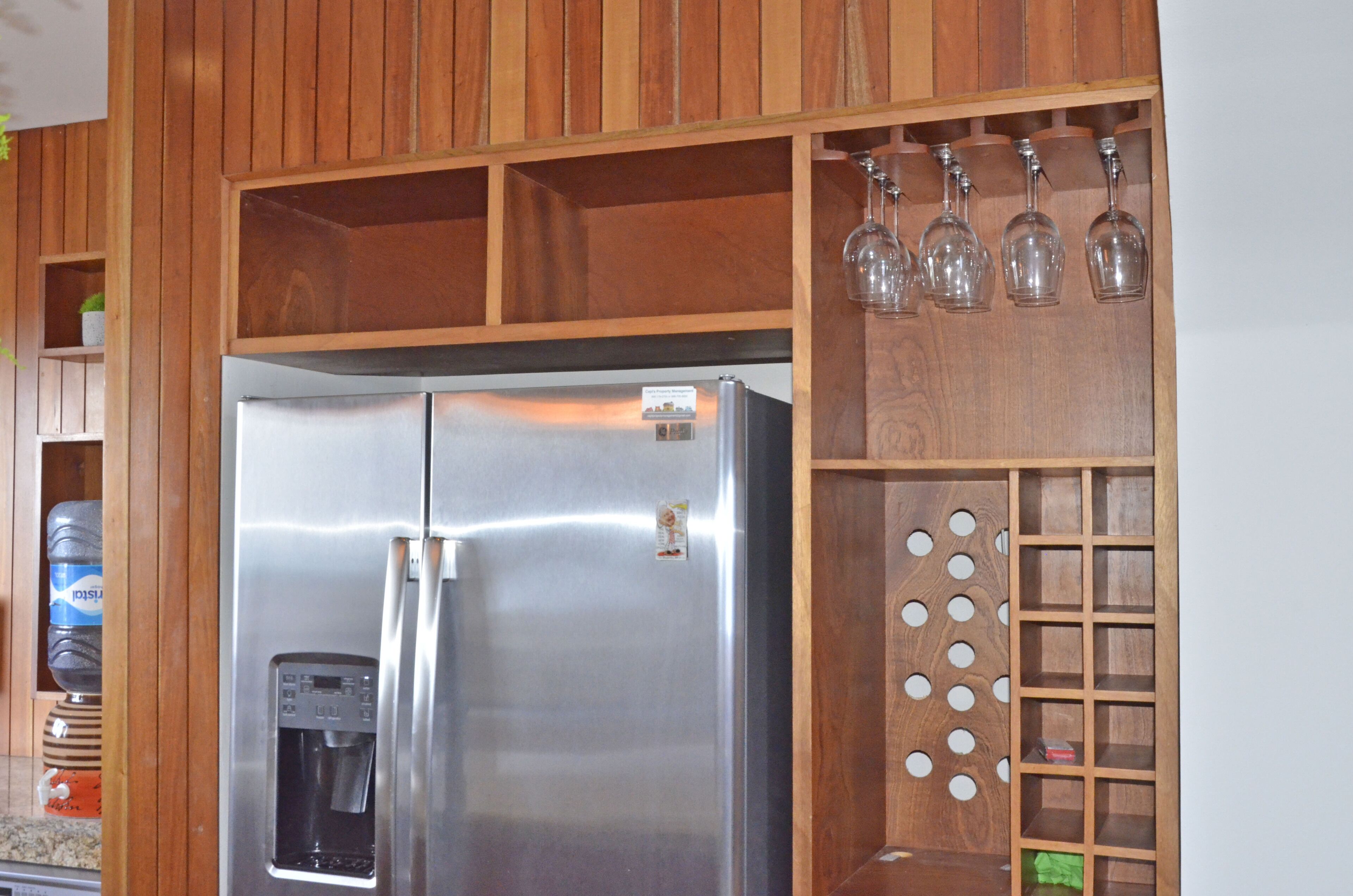 A stainless steel refrigerator with a water dispenser, wooden paneling, and a wine rack with glasses.