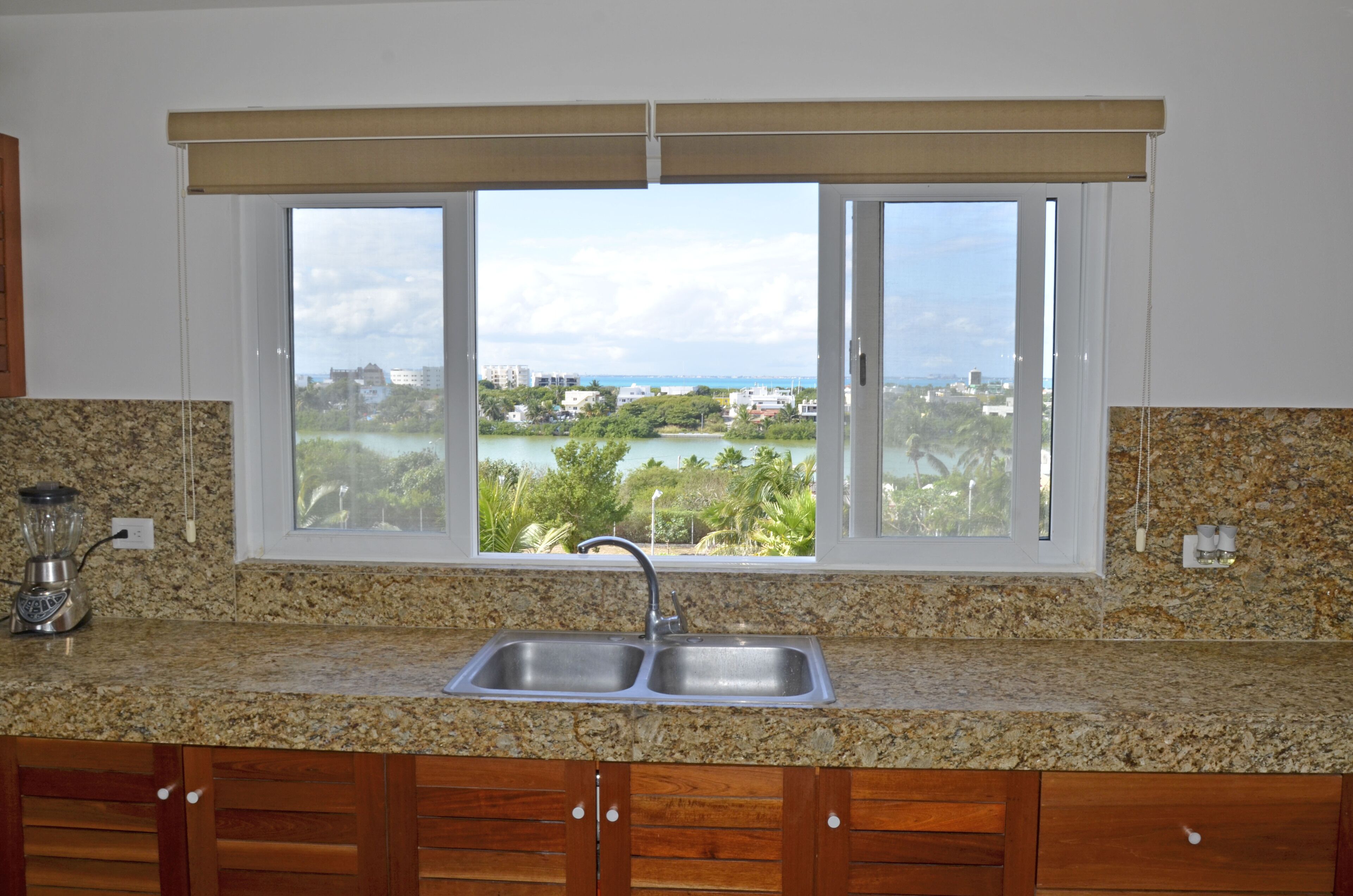 A kitchen with granite countertops, a double sink, wooden cabinets, and a window with a view of a cityscape and greenery.