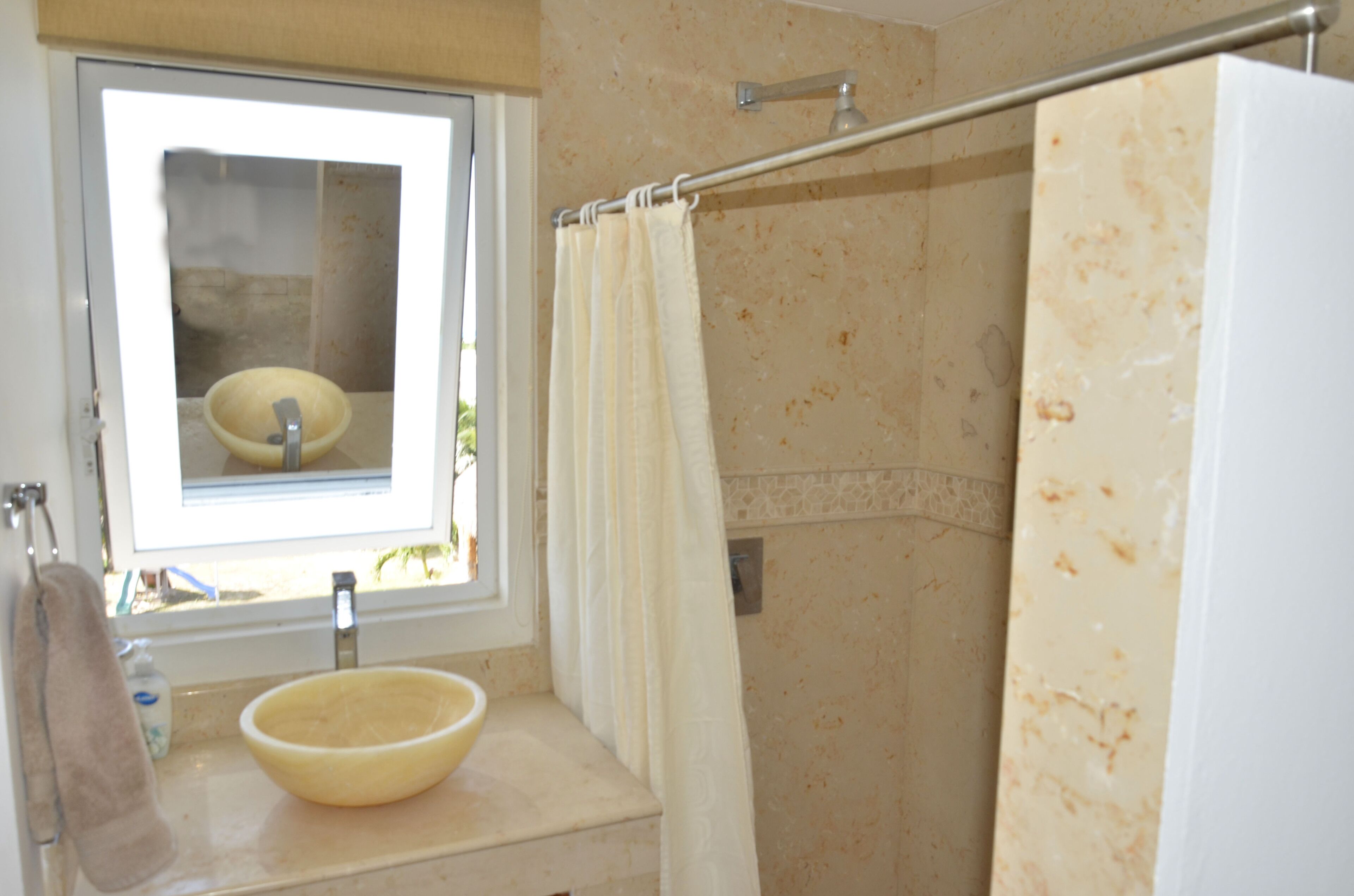 A bathroom with a window, a sink with a bowl, and a shower curtain.