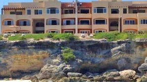 Een kusthotel met meerdere balkons, een rotsachtige kustlijn en een helder uitzicht op de oceaan.