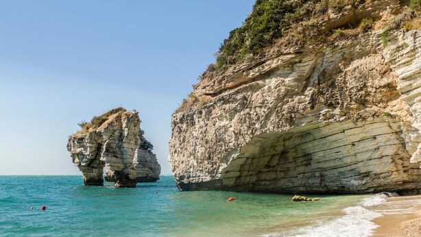 A coastal landscape with rocky cliffs and clear turquoise waters.