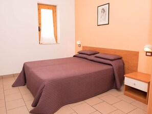 A bedroom with a bed, a nightstand, a wall-mounted lamp, a window with a curtain, and a framed picture on the wall. - Apartment in the Gargano Park (Vieste)