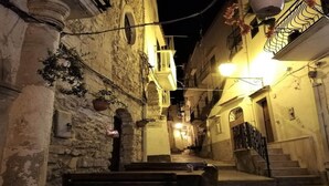 A narrow street with stone buildings, outdoor seating, and a staircase leading to a second floor.