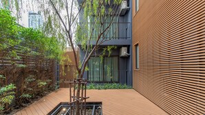 A modern building with a wooden slatted facade, a small garden area with a wooden structure, and a metal fence. - GROOVE AT SIAM (Bangkok)