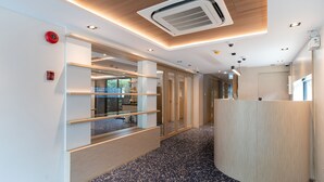 A modern reception area with a wooden reception desk, glass shelving units, and a ceiling-mounted air conditioning unit. - GROOVE AT SIAM (Bangkok)