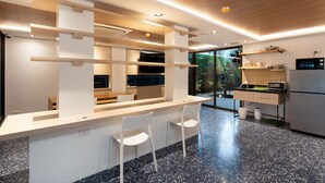 A modern kitchen with a bar area, white chairs, and a view of the outdoors. - GROOVE AT SIAM (Bangkok)