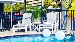 A poolside area with white lounge chairs, a small table with drinks, and two white floating balls.