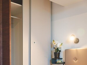 Ein modernes Badezimmer mit Holztür, weißer Wand, schwarzem Regal mit Topfpflanze und einer runden Leuchte.