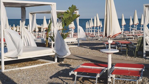 A beachside hotel with white cabanas, red lounge chairs, and umbrellas.