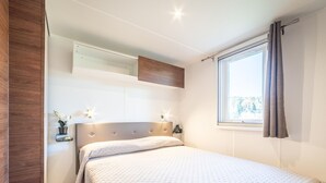 A bedroom with a bed, bedside tables, a window with curtains, and a wall-mounted shelf with a plant.