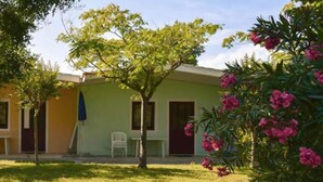 A building with a green facade, a small garden with a tree and pink flowers, and a white chair outside. - Belvilla by OYO Villini a Schiera (Altidona)
