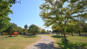 A park with a gravel path, playground equipment, and trees. - Belvilla by OYO Villini a Schiera (Altidona)