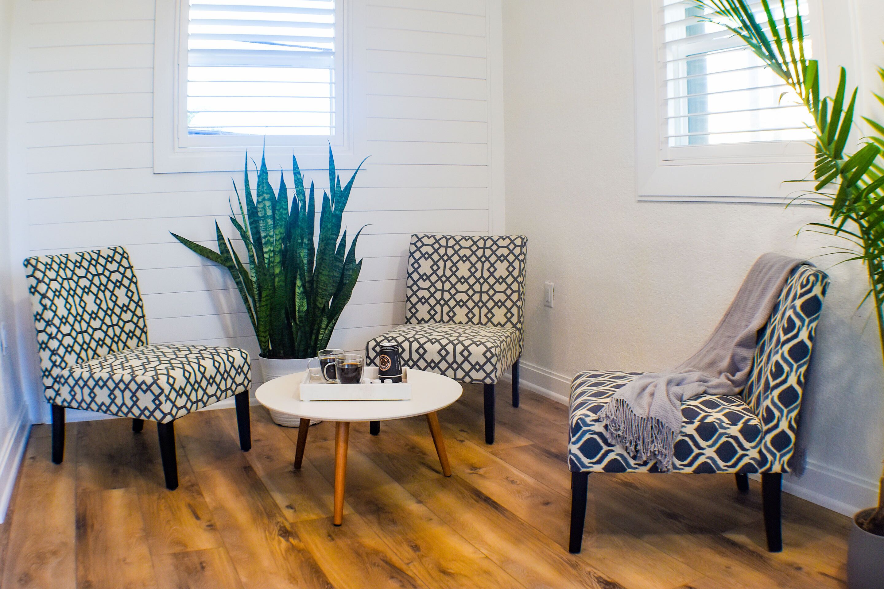 Una habitación con dos sillones estampados, una mesa redonda con una bandeja de objetos y una planta grande.