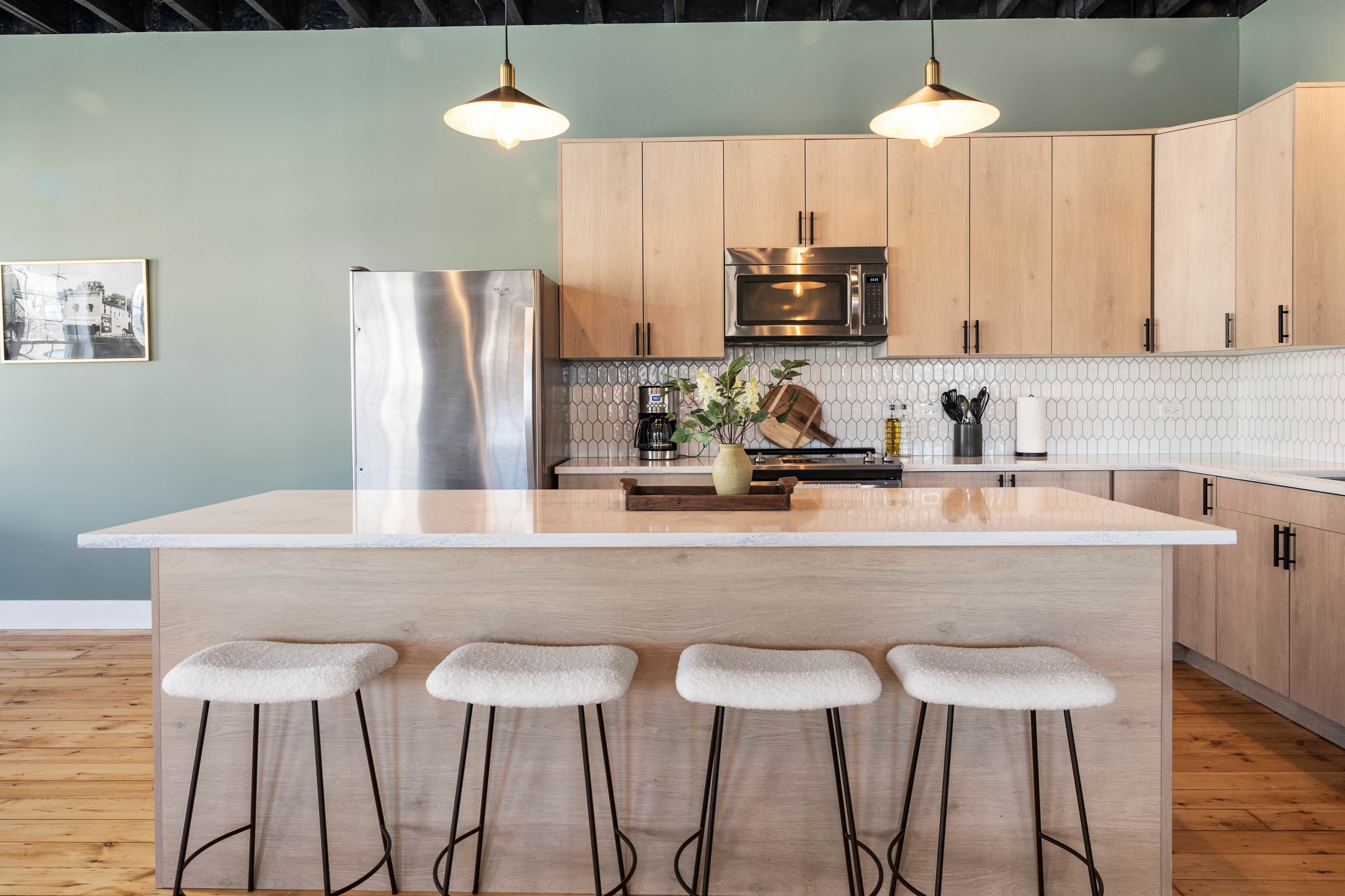 Una cocina moderna con armarios de madera, un refrigerador de acero inoxidable, un microondas y una isla grande con taburetes de bar.
