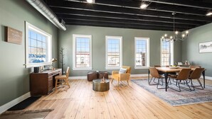 A spacious room with a wooden floor, a dining table with chairs, a fireplace, and large windows.