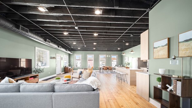 A spacious living area with a grey sofa, wooden flooring, and a kitchen area with a bar.