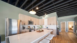 A modern kitchen with a large island, stainless steel appliances, wooden cabinets, and pendant lighting.