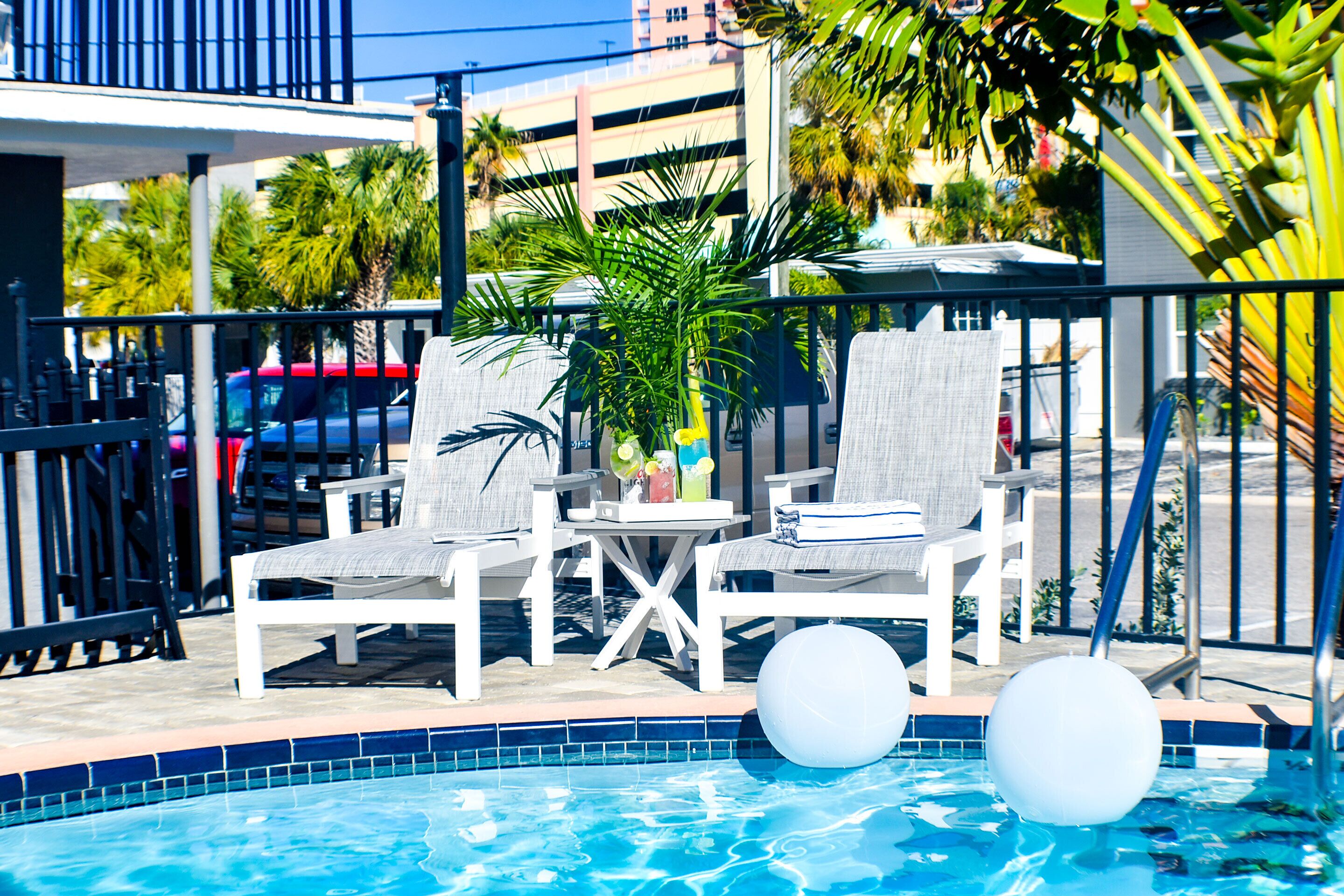 A poolside area with white lounge chairs, a small table with drinks, and two white floating balls.