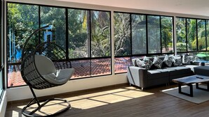 A modern living room with large windows, a grey sofa set, a black rocking chair, and a wooden coffee table. - Private Beach side Home - Playa San Diego (La Libertad)