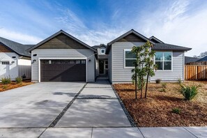 A two-story house with a garage, a front yard with mulch and a small tree, and a clear blue sky. - Boho Betty (Windsor)