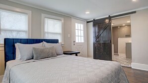A bedroom with a large bed, a dark headboard, and a view of a bathroom through an open door. - Blue Horizon Retreat- Near Downtown McKinney  (McKinney)