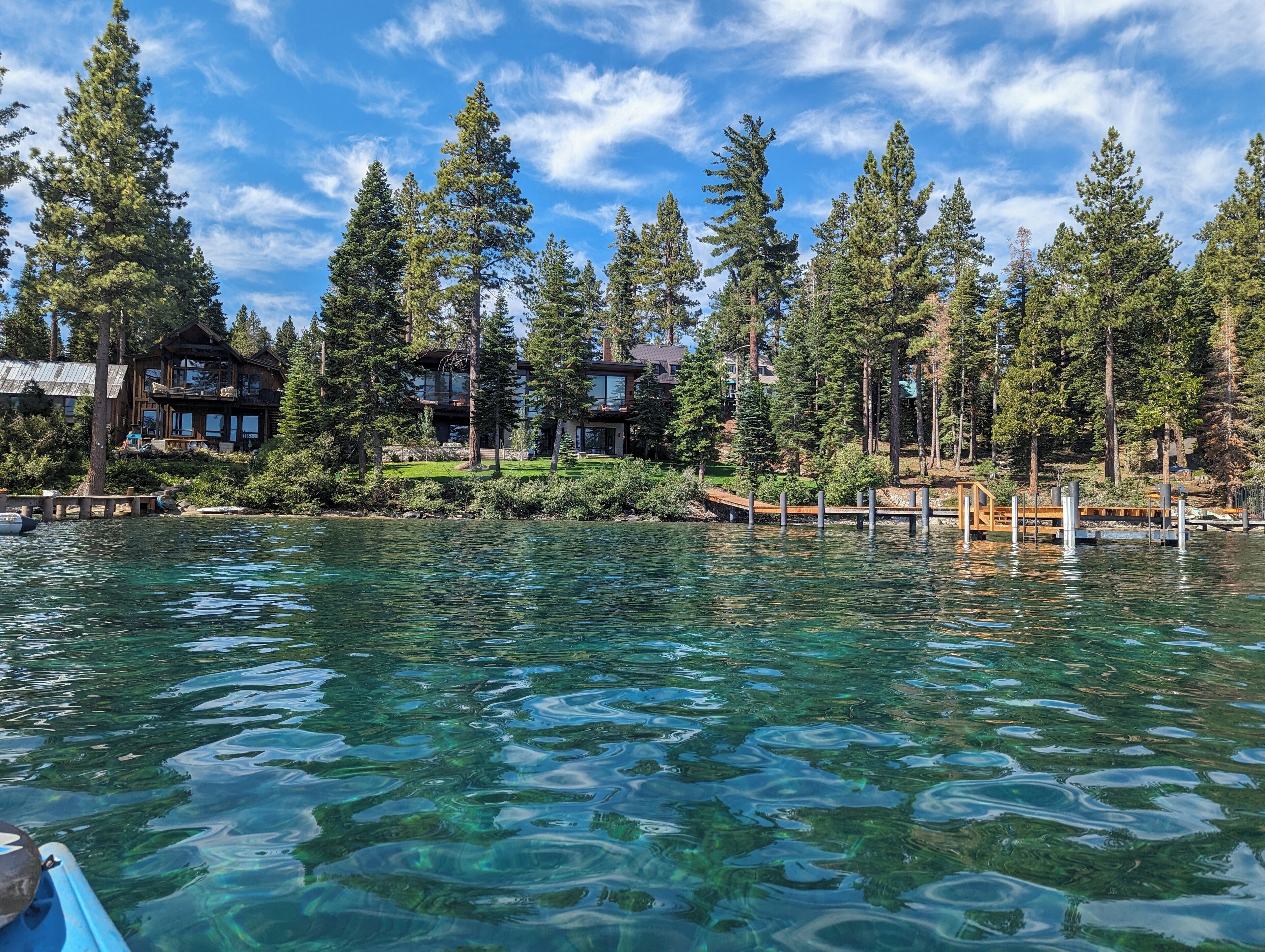 A lakeside property with multiple wooden cabins, clear water, and surrounding tall pine trees.
