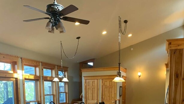 A spacious living area with a large sofa, two armchairs, a dining table, and a kitchen area with wooden cabinets and a ceiling fan. - Private Lakefront with Dock! (MONGAUP VALLEY)