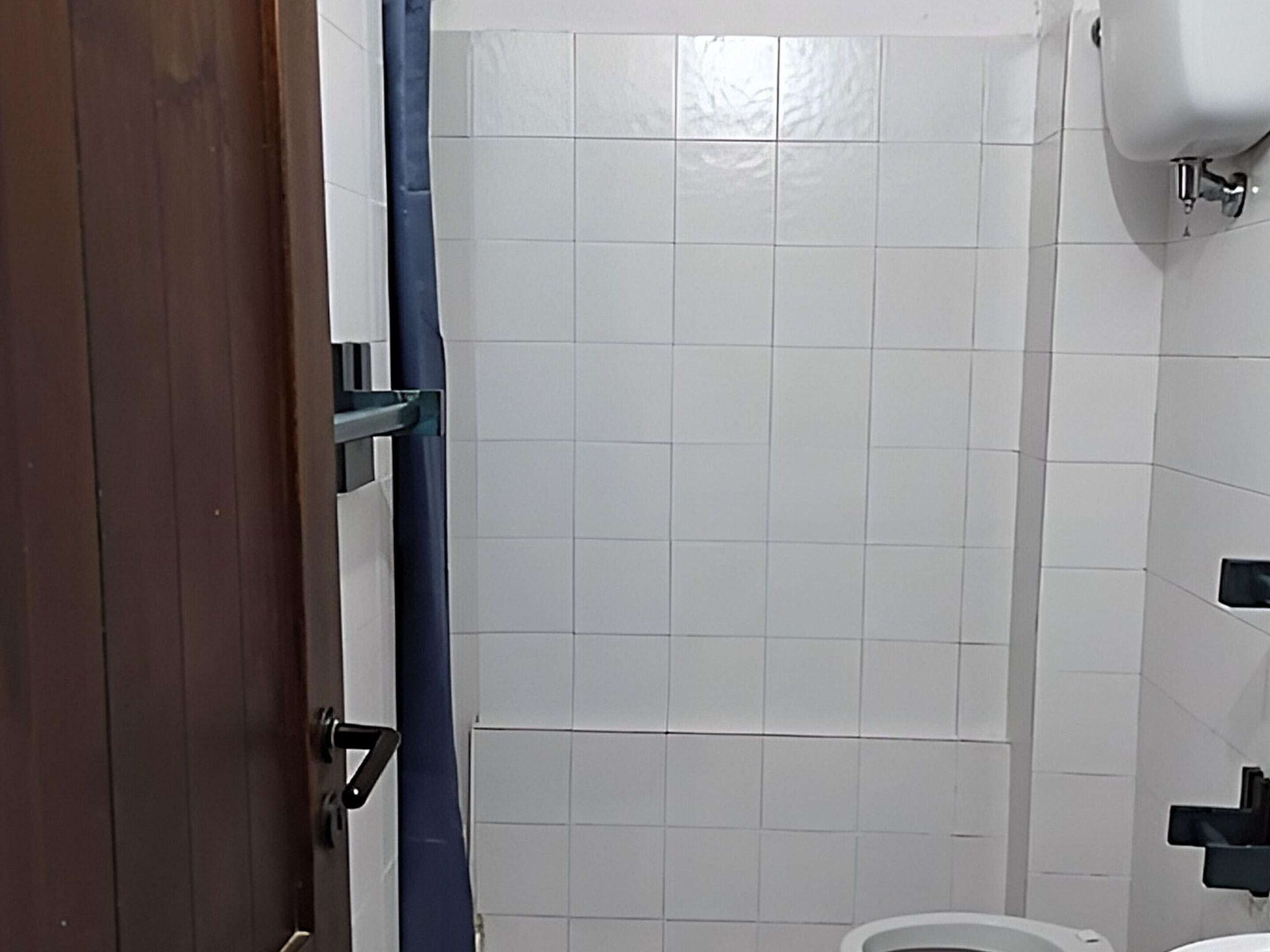 A bathroom with white tiled walls, a white toilet, and a blue shower curtain.