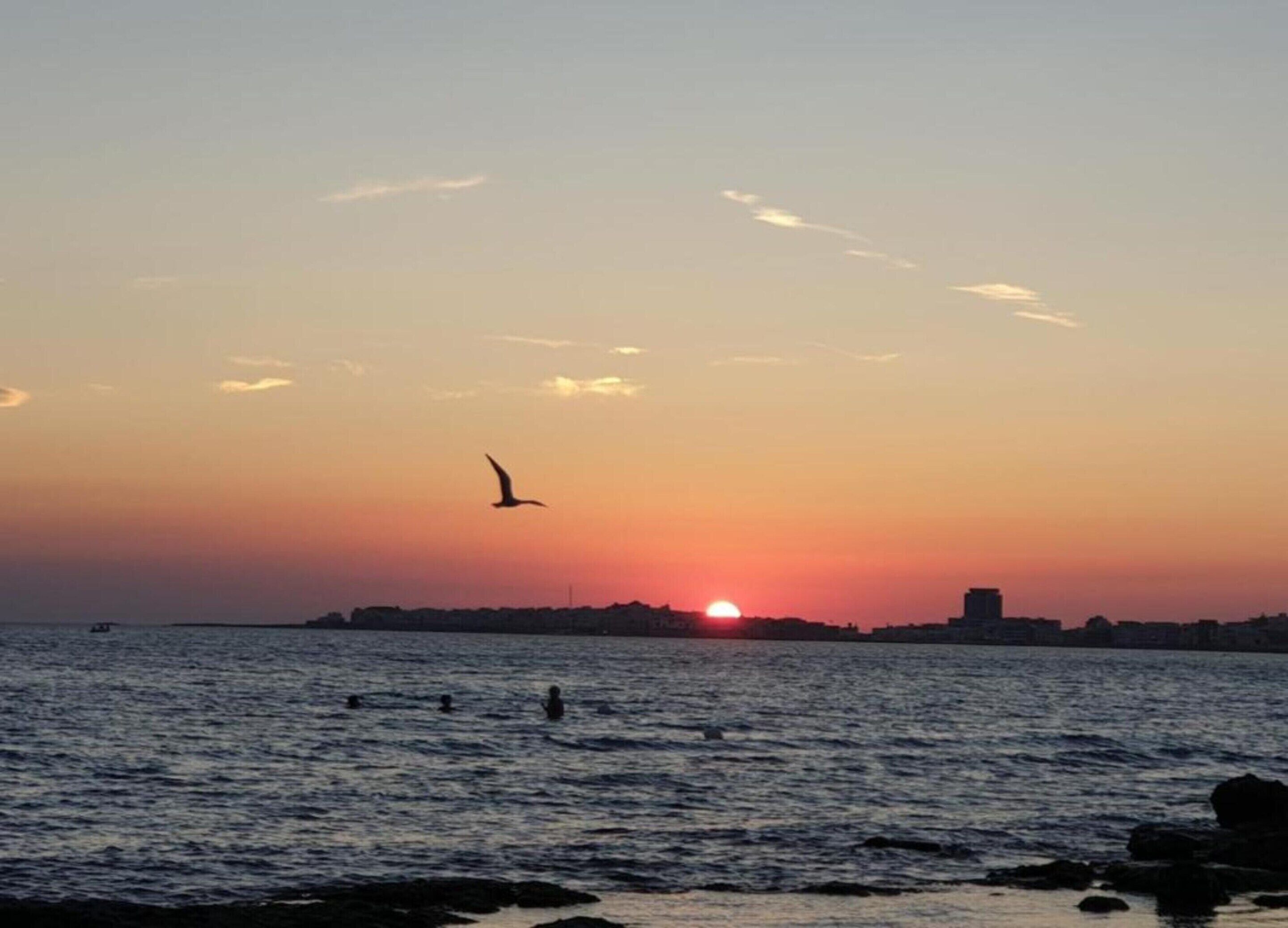 A sunset over a body of water with a silhouette of a city skyline in the background.