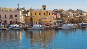 A harbor with several boats docked, a prominent yellow building with a tower, and a variety of other buildings in the background. - Apartment Marina di Mancaversa by Ionian Sea (Taviano)