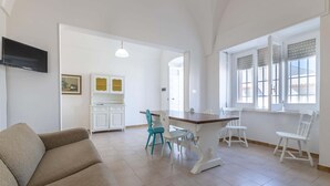 A spacious living area with a sofa, a dining table with chairs, a kitchen in the background, and a TV mounted on the wall. - Apartment Marina di Mancaversa by Ionian Sea (Taviano)