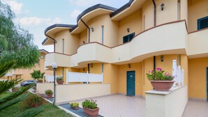 Un edificio de varios pisos con fachada curva, plantas en macetas exteriores y una entrada protegida por una reja.