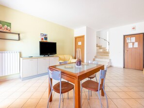 Ein Essbereich mit Tisch, Stühlen, einem Fernseher, einem Heizkörper, einer Couch und einer Treppe.