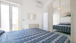 Ein Schlafzimmer mit einem großen Bett, einem Kleiderschrank, einem Spiegel und einer Tür zu einem Außenbereich.