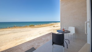 Ein Balkon mit Blick auf Strand und Meer. Ein Tisch mit zwei Stühlen und einer Weinflasche sind vorhanden.