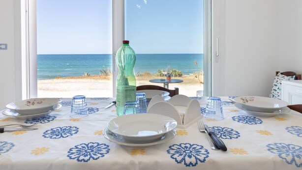 Ein Esstisch mit Blick auf den Strand und das Meer durch ein großes Fenster.