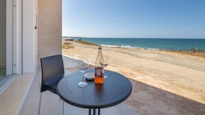 Ein Balkon mit Tisch, Stuhl, Flasche und Glas. Blick auf einen Strand und den Ozean.