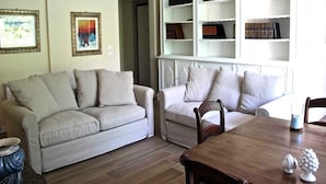 A living room with two sofas, a wooden table, and a bookshelf filled with books. - Holiday Home in Reggio Calabria Near Beach (Reggio Calabria)