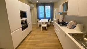 A modern kitchen with white cabinets, a built-in oven, and a dining area with a table and chairs. - Holiday Home in Reggio Calabria Near Beach (Reggio Calabria)