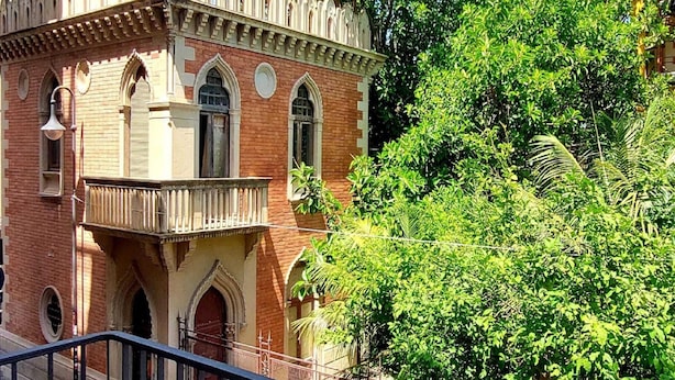 A historic building with arched windows and a balcony, surrounded by lush greenery. - Holiday Home in Reggio Calabria Near Beach (Reggio Calabria)