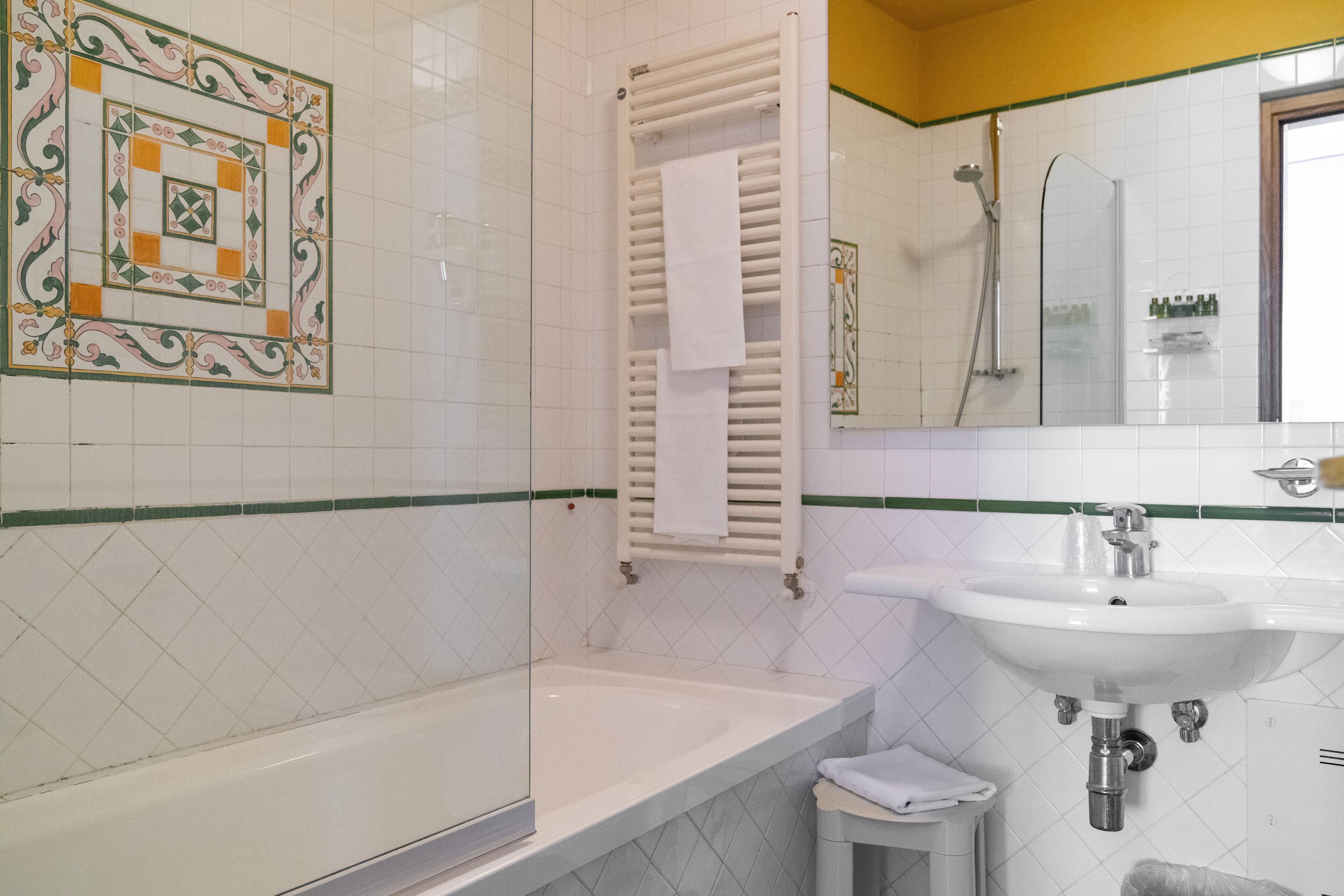 Un baño con bañera, lavamanos, ducha con mampara de vidrio y un perchero para toallas.