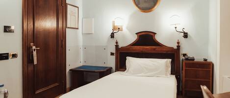 A hotel room with a wooden bed, a nightstand, a desk, a chair, a water bottle, and a door.