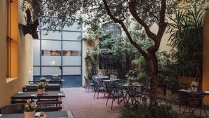An outdoor café with tables and chairs, surrounded by potted plants and trees. - Il Guelfo Bianco (Florence)