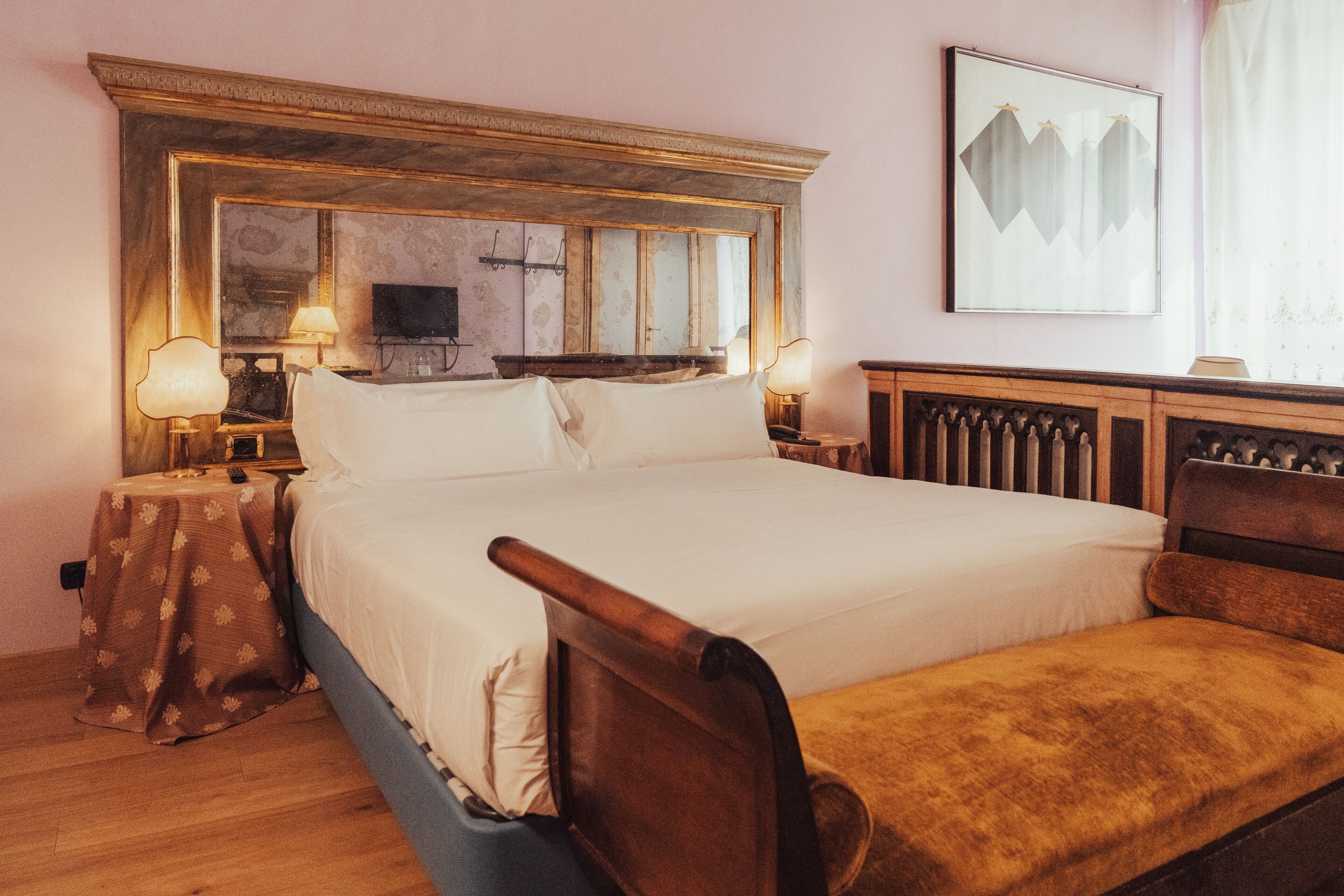 Una camera da letto con un letto grande, una testiera in legno, comodini con lampade, un tavolino con tovaglia fantasia e un quadro appeso al muro.