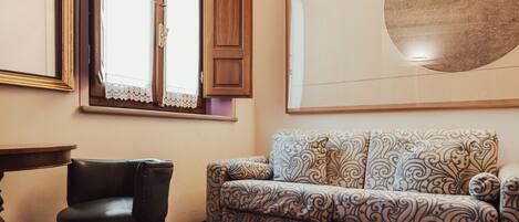 A room with a patterned sofa, a wooden chair, a round mirror, and a large abstract artwork on the wall.