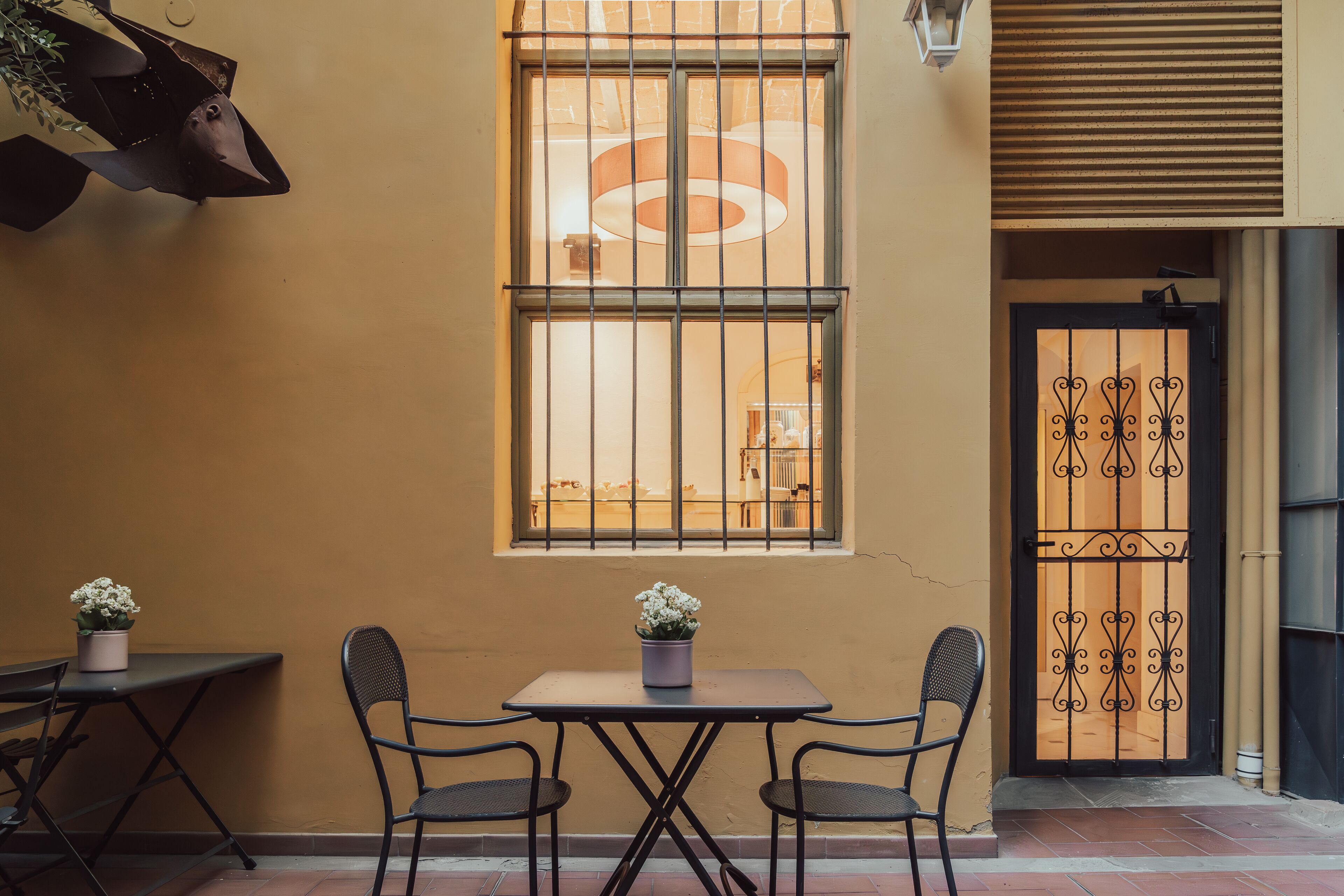 Un petit espace extérieur aménagé avec une table et deux chaises, un pot de fleurs et une fenêtre à carreaux.