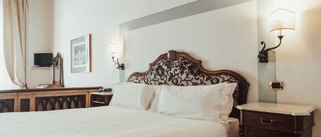 A neatly made bed with white linens, a wooden headboard with a floral pattern, and two wall-mounted lamps.
