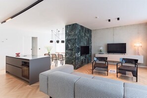 Un salon moderne avec un mur d’accent en marbre, un téléviseur à écran plat et un coin repas comprenant des chaises et un petit îlot.
