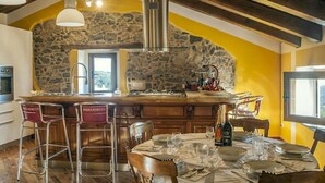 A kitchen with a stone wall, wooden beams, and a dining area with a table set for four.